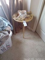 Round table with light-colored top and gold metal legs, viewed from the side with miscellaneous items on top.