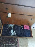 Top view of opened wooden drawer filled with folded female clothes including dark blue, pink, and black items.