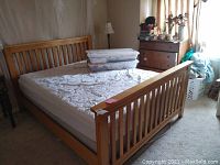 Wooden queen size bed frame with slatted headboard and footboard, adjustable Tempurpedic mattress on top, seen in a bedroom setting.