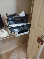 HP printer with black plastic document trays containing various office supplies, including pens, light bulb, calculator.