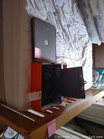 Photo showing Dell laptop on bed with box containing charging cords, small black speakers, clipboard, and pins in a cup