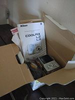 Box containing Nikon Coolpix L2/L3 user manuals, camera and paperwork