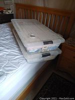 Two large clear plastic bins stacked on a bed with baby clothes and blankets inside, showing storage method.