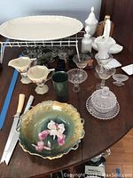 Full view of assortment including large ceramic platter, porcelain bowl with floral design, milk glass items, cream and sugar set, glassware, and cutlery.
