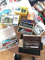 Overview photo showing multiple model building kits, X-ACTO knife sets, glue tray, and H O scale train layout pieces on a table.