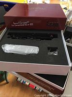 Open red Paragon series box with foam insert showing one black steam locomotive and wrapped accessories