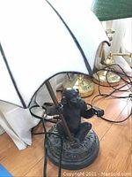Full view of monkey lamp base holding pole with umbrella-shaped acrylic shade. Black monkey figure on circular decorated base.