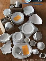 Overview of all dishes and dinnerware stacked and boxed on wooden floor, showing plates, bowls, mugs, serving pieces.