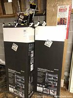 Photo showing three boxed 5-tier adjustable steel shelves stacked upright with six white-ended overhead storage hooks placed on top.