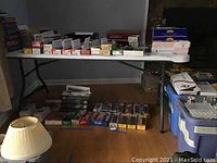 White folding table in a room, with various boxes and items placed on and around it (items not included).
