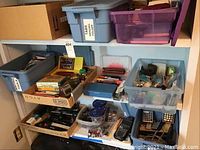 Three shelves holding assorted office supplies including staplers, pens, pencils, scissors, small tools, and storage bins.