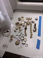 Wide shot showing assorted costume jewelry spread on a white surface, including earrings, bracelets, necklaces, pins, and a metal spoon.