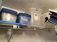 Plastic storage containers on wire closet shelf, including blue and clear Rubbermaid Keepers containers, white bin, and other assorted containers.