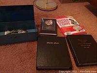 Overview of the coin books, coin collecting books, and postcards with loose coins in a box.