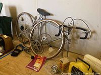 Side view of Silver Shadow road bicycle with 27 inch wheels, dropped handlebars and accessories sitting on floor by wall.