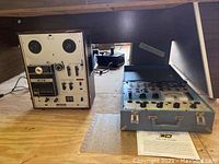Two units side by side on floor: left Akai tape recorder, right gray metal tube tester in open carrying case, paper manual in front