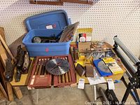 Wide view of lathe tools, saw blades, and woodworking accessories displayed on shelves and tables in garage setting.