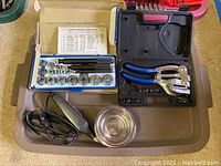 Tray with punch plier tool with blue handles, socket set in blue box, electric soldering iron, and small metal bowl