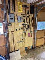 Pegboard with assorted hammers, rubber mallets, pry bars, hacksaw frame, torpedo level, paint brush and shovel