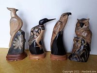 Four horn bird carvings arranged side by side, showing front view of each carving on wood bases except one.