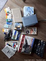 Photo showing two Dremel rotary tools, various accessories including sanding discs, drill bits, colorful packaging, two carrying cases (one blue, one gray) and several manuals/booklets spread on the floor.