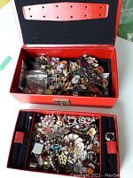 Overview of red jewelry box opened showing mixed assortment of jewelry items including single earrings, pendants, and jewelry components.