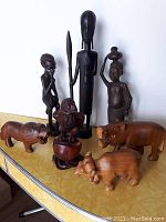 Seven wood carvings including human and animal figures displayed on a surface.