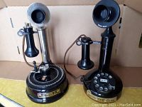 Pair of vintage reproduction telephone bottles with telephone style bases, one with a silver earpiece and one with a black earpiece.