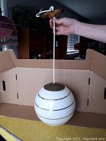 Full view of the spherical white glass globe light fixture showing the top metal canopy and white suspension cord held by a hand.