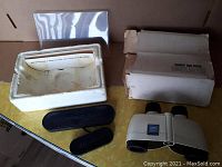 Photo of vintage Bushnell Expo binoculars with original box, styrofoam insert, and lens covers laid out on a table.