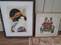 Both framed oriental pictures displayed side by side on the floor against a wall