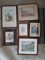 Six vintage framed pictures arranged on floor showing various architectural and coastal scenes.