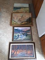View of all four framed landscape paintings laid on floor, showing variety of scenes and frames