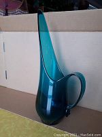 Full side view of vintage blue/turquoise glass pitcher showing tall narrow spout and round base with handle.