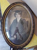 Front view of oval framed black and white portrait of a young woman in graduation attire.