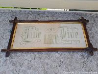 Full view of framed needlepoint motto showing gothic lettering and decorative frame