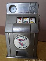 Front view of vintage dime slot machine bank showing coin slot marked 10 cents, three spinning reels, and Las Vegas Nevada cartoon cowboy logo.