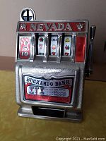 Front view of the Buckaroo Bank vintage slot machine coin bank showing the Nevada sign, reels with symbols, and coin slot.