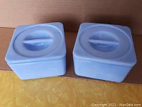 Pair of light blue Jeannette Glass fridgies with lids viewed from top showing circular handle and minor chips.