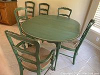 Full view of green painted oval table with six rush seat ladder back chairs, including two armchairs.