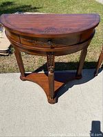 Front view of demi-lune table showing curved half-moon shape, drawer with floral carvings, and three legs with decorative details.