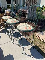 Three green metal bar stools arranged outside. Showing tall back supports and round upholstered seats with floral bird pattern.