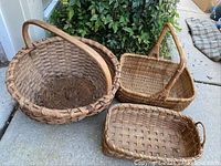 Three antique woven baskets displayed on ground against greenery, showing different shapes and sizes.