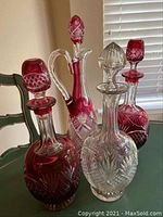 Photo showing all four cut glass decanters on a green table against blinds and a chair in the background.