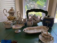 Wide shot showing entire porcelain collection on green table by window.