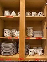 Kitchen cabinet shelves with stacks of dinner plates, salad plates, bowls, cups, mugs, creamer, and sugar bowl all in Petit Fleur pattern porcelain.