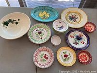 Wide view showing assortment of plates and bowls with varied floral patterns and colors including some small custard bowls and larger decorative plates.