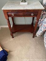 Full front view of antique wooden side table with white marble top and lower shelf on carpeted floor.