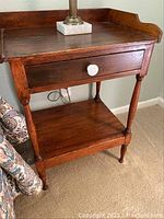 Front view of antique wooden wash stand showing single drawer with white ceramic knob and lower shelf.