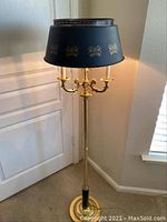Full view of brass floor lamp showing tole shade with decorative gold fleur-de-lis pattern and candle-style bulb holders.
